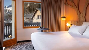 Una habitación de hotel con una cama grande, una mesita pequeña, un ventanal con vista a una montaña y una pared de madera.