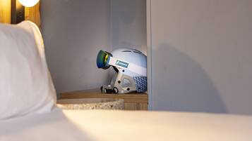 Een hotelkamer met een bed, een bedlamp, een wandplank met een plant, een koffer en een stofzuiger.