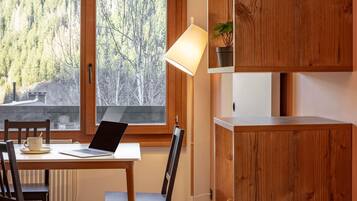 Un interior de madera con una mesa, sillas, una computadora portátil, una lámpara y un ventanal con vistas a árboles.