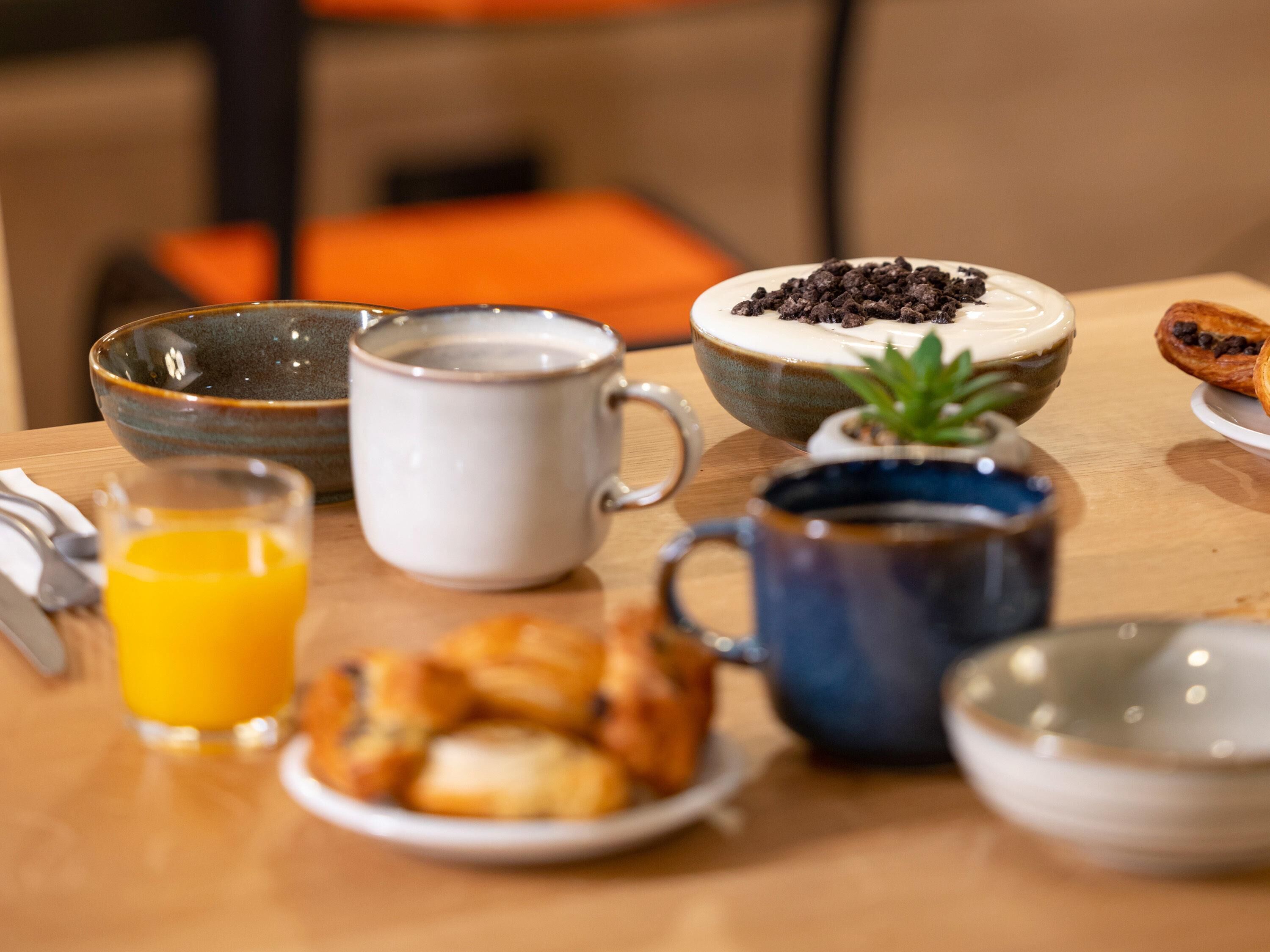 Une table de petit-déjeuner avec un bol de céréales, une tasse de café, un verre de jus d’orange et une assiette de viennoiseries.