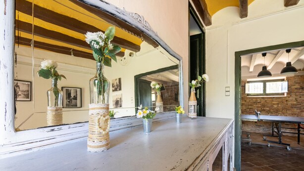 Un intérieur rustique avec un comptoir en bois où sont exposés des vases de fleurs, un grand miroir qui reflète la pièce et un mur de briques en arrière-plan.