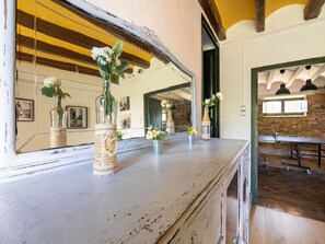 A rustic interior with a wooden counter displaying vases with flowers, a large mirror reflecting the room, and a brick wall in the background.