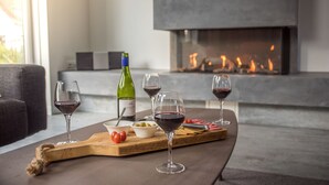 Ein modernes Wohnzimmer mit Kamin, einem Holztisch mit Weingläsern, einer Weinflasche und einer Oliven-Schale.