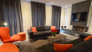 Ein modernes Wohnzimmer mit einer Sofagarnitur, orangefarbenen Sesseln, einem Couchtisch und einem an der Wand befestigten Flachbildfernseher.