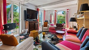 Un salon spacieux doté d’un grand téléviseur à écran plat, de sièges confortables et offrant une vue sur la verdure environnante.