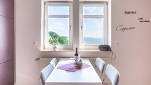A dining area with a white table, four chairs, a bottle, and a bag of snacks. Two windows offer a view of greenery and a body of water. - Wohnung in Battenberg nahe Winterberg Skigebiet (Battenberg)