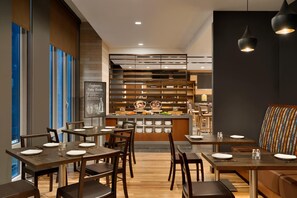 Een modern restaurant met houten tafels en stoelen, een toonbank met een menu en een zithoek met een kleurrijke bank.