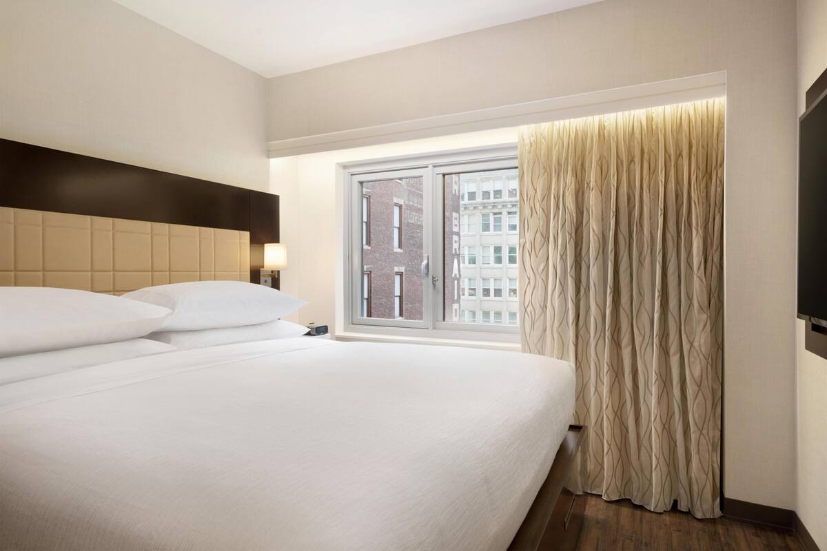 Une chambre d’hôtel avec un grand lit, une fenêtre avec des rideaux et une vue sur les bâtiments environnants.