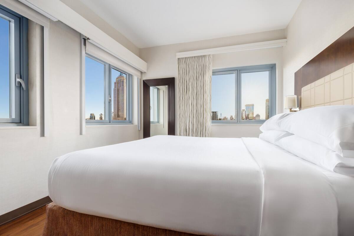 Une chambre d’hôtel avec un grand lit, deux fenêtres, une vue sur la ville et une porte.