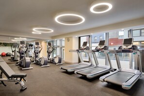 Ein Fitnessstudio mit Laufbändern, Crosstrainern und einer Bank.