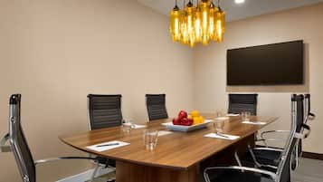 Un salón de conferencias con una mesa de madera, seis sillas, un plato de fruta y un televisor montado.