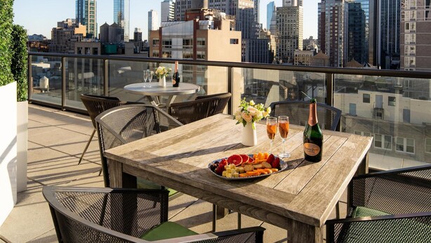 A rooftop terrace with a table set for dining, a bottle of champagne, and a city skyline view. - Embassy Suites by Hilton New York Manhattan Times Square (New York)
