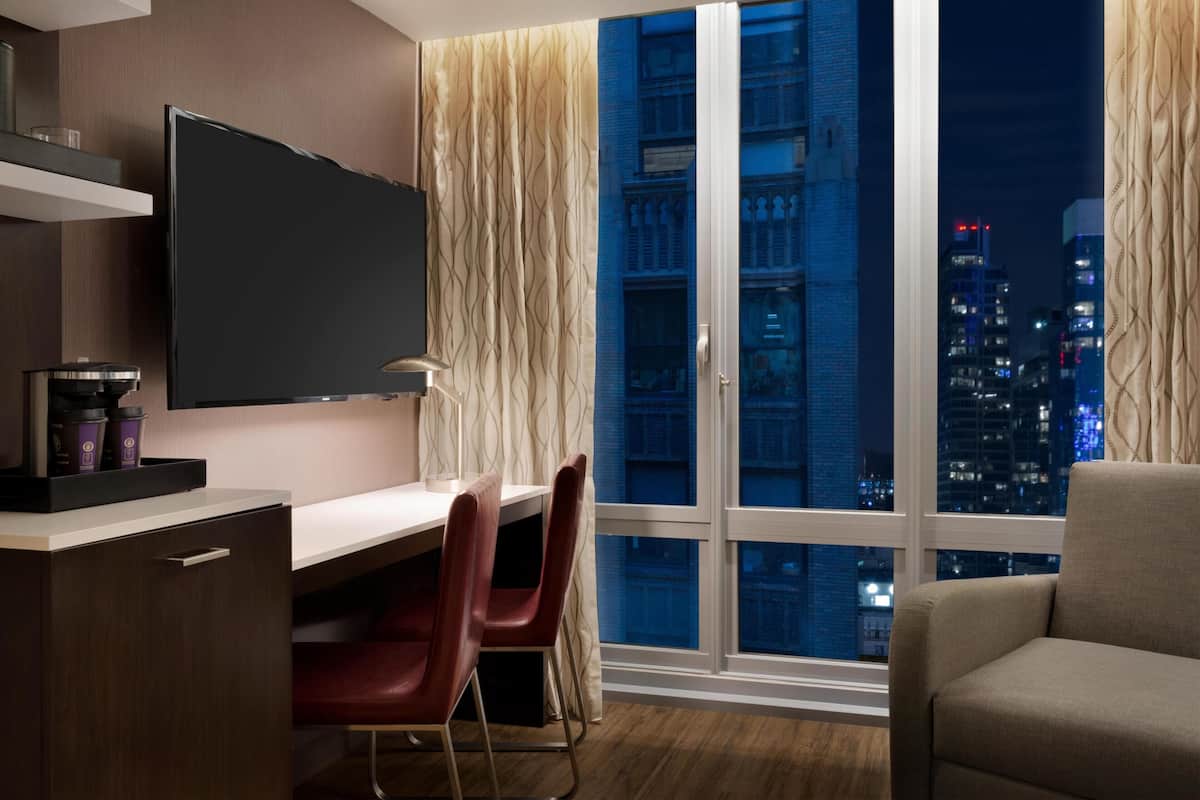 Une chambre d’hôtel moderne dotée d’une grande télévision, d’un bureau avec des chaises, d’un canapé et offrant une vue sur la ville.
