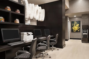Un espace de bureau moderne doté de plusieurs postes de travail, d’une grande œuvre d’art abstraite et d’un coin cuisine.