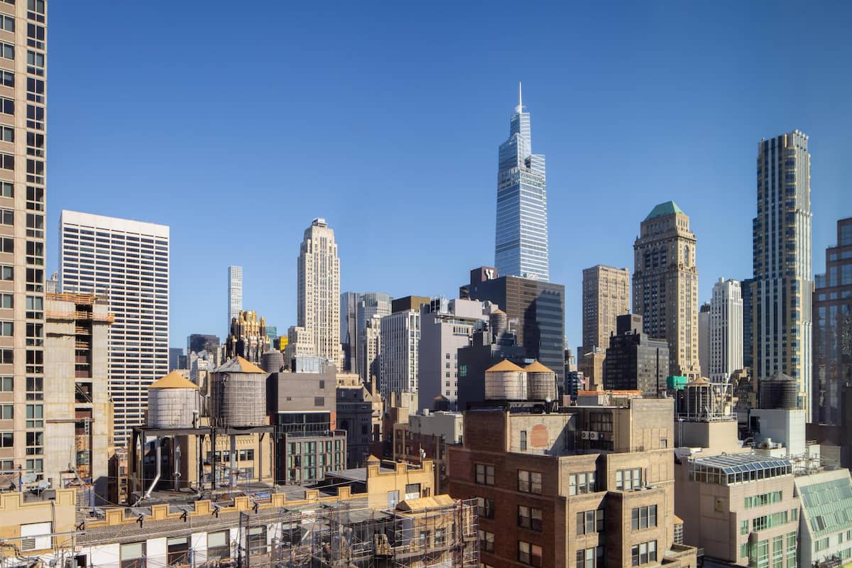 Un paysage urbain caractérisé par de nombreux immeubles de grande hauteur, dont un gratte-ciel remarquable surmonté d’une flèche, et une diversité de styles architecturaux.