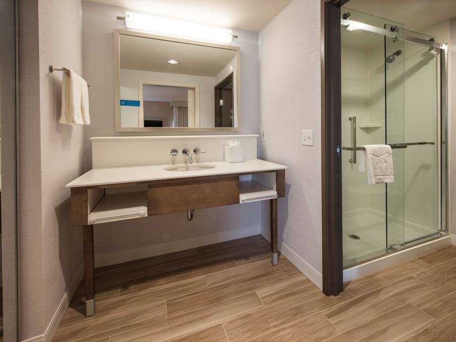 Une salle de bain moderne avec un meuble-lavabo en bois, un grand miroir, une douche en verre et un lavabo blanc.