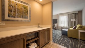 A modern hotel room with a kitchenette, a large window with curtains, a sofa, and a flat-screen TV. - Hampton Inn & Suites Seattle/Redmond (Redmond)