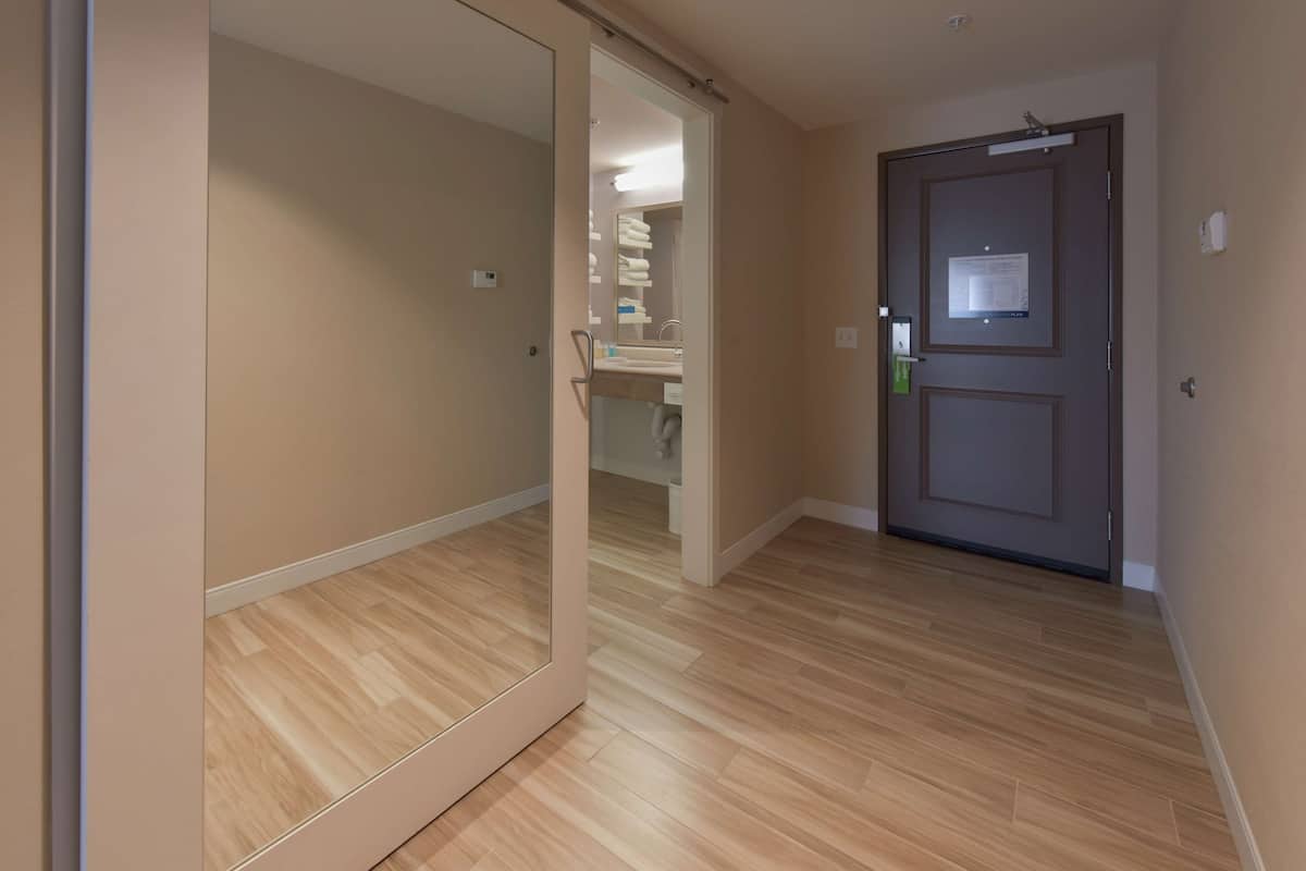 A hallway with a wooden floor leading to a door with a bulletin board.