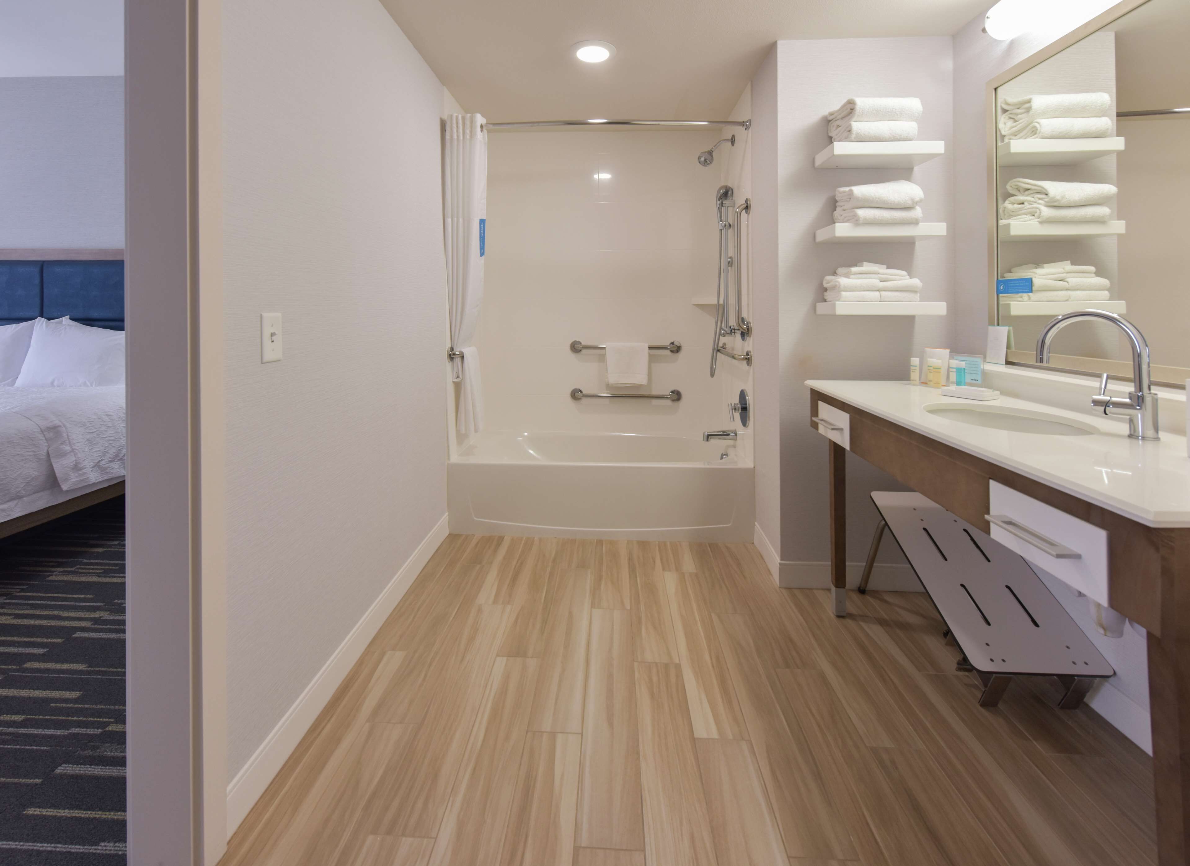 A modern bathroom with a bathtub, shower, and a vanity with a mirror and towel rack.