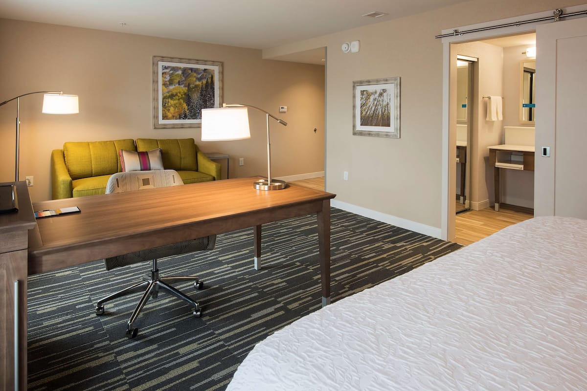 A hotel room with a bed, a desk, a chair, two lamps, and two framed pictures on the wall.