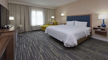 A hotel room with a large bed, a desk, a chair, a TV, and a window with curtains.