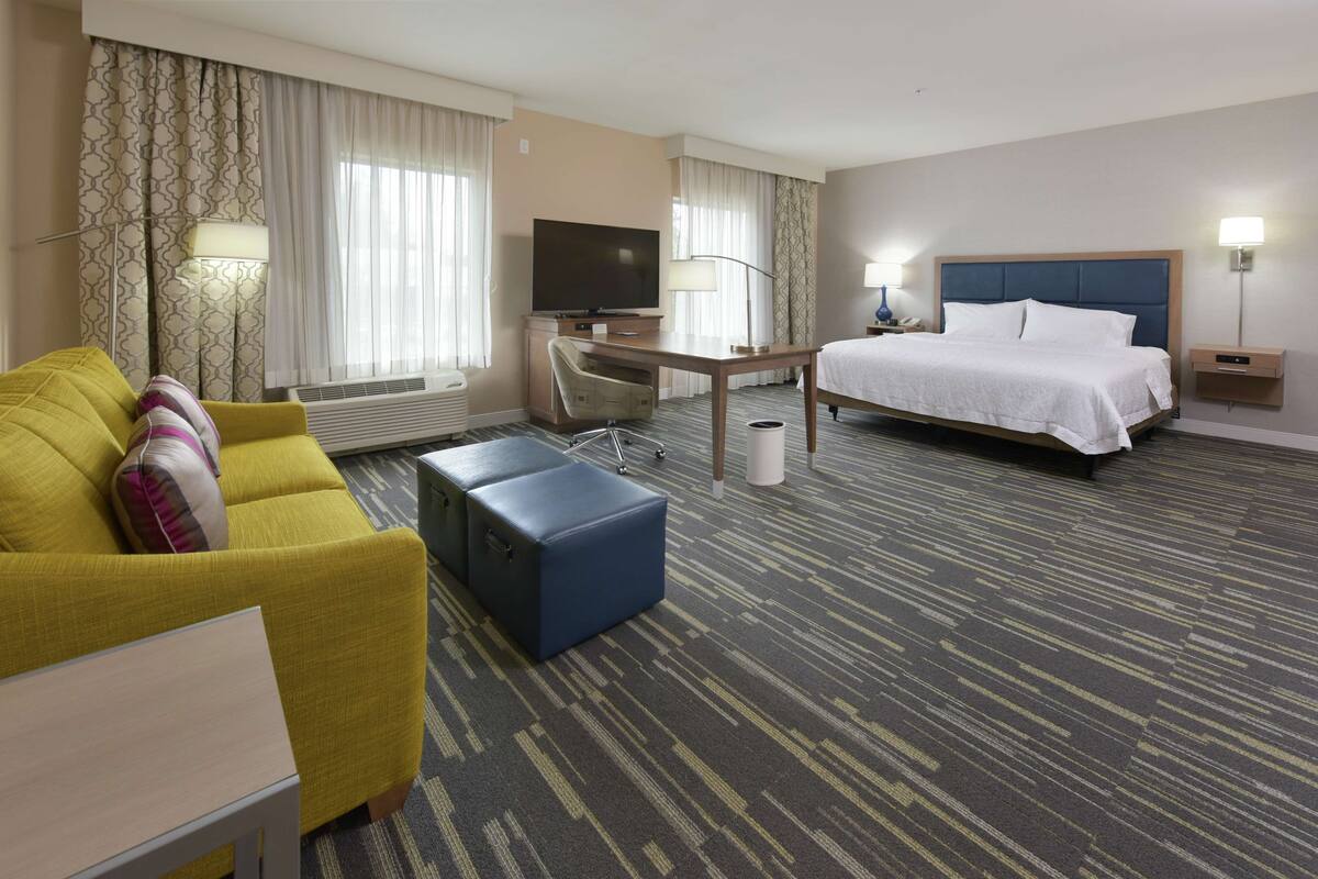 A hotel room with a bed, a desk, a TV, a sofa, and a chair.