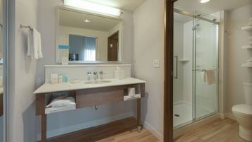 A modern bathroom with a glass shower enclosure, a white sink with a mirror above, and a wooden vanity.