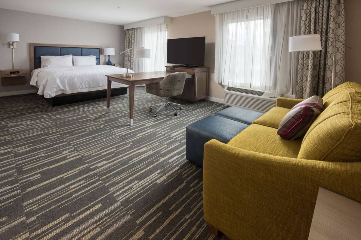 Een hotelkamer met een bed, bureau, televisie en een geel slaapbank.