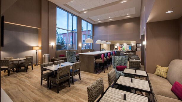 A modern dining area with tables and chairs, a bar area, and large windows offering a view of the outside. - Hampton Inn & Suites Seattle/Redmond (Redmond)