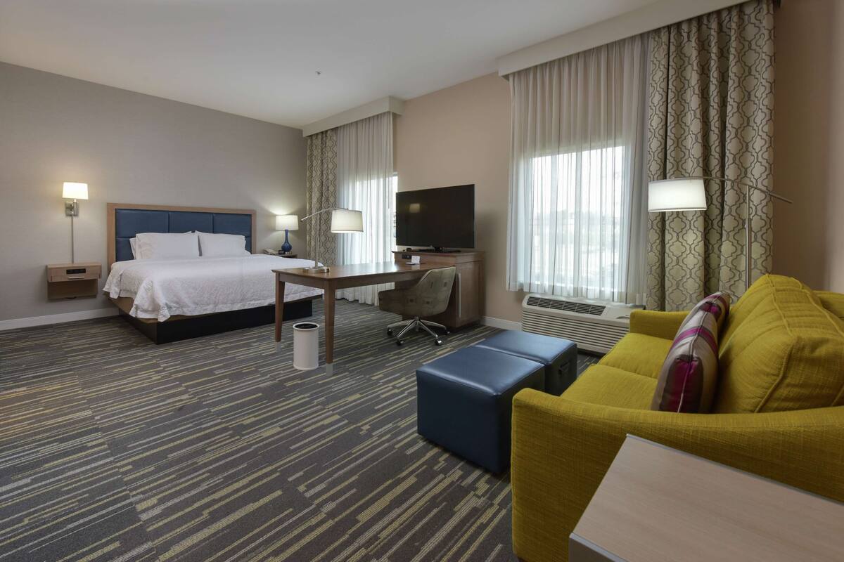 A hotel room with a bed, a desk, a television, a sofa, and a lamp.