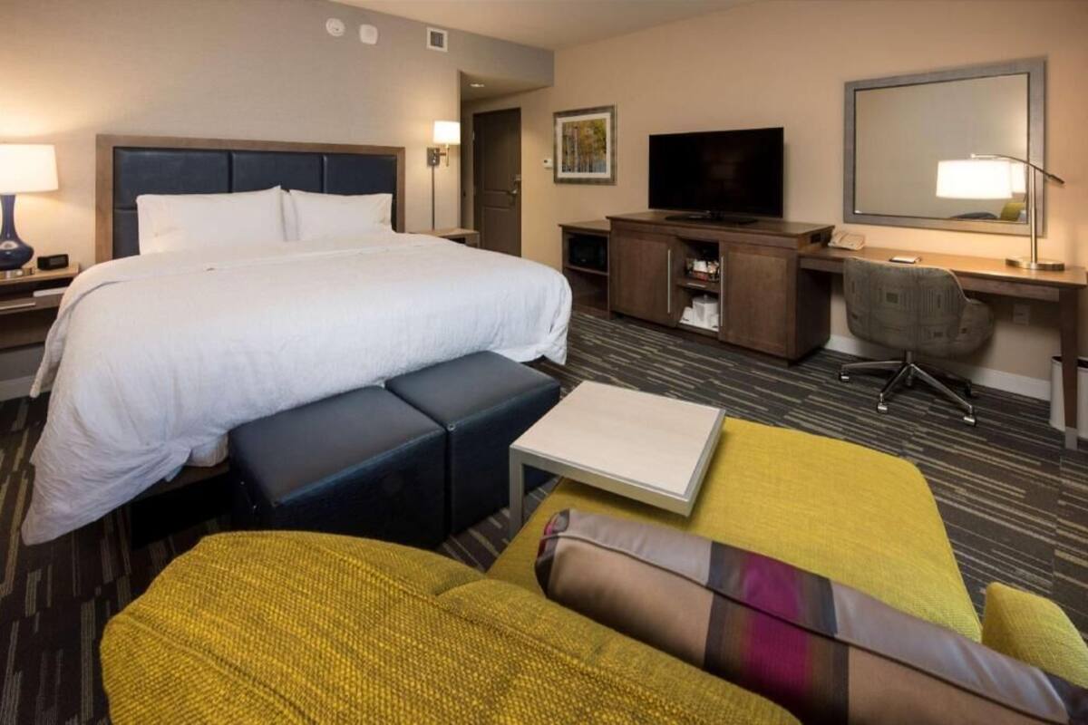 A hotel room with a large bed, a desk with a chair, a television, and a mirror.