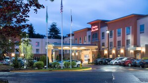 A Hampton Inn & Suites hotel with a parking lot, flagpoles, and a well-lit entrance. - Hampton Inn & Suites Seattle/Redmond (Redmond)