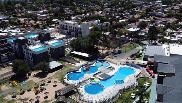 An aerial view of a resort with a large pool area, multiple buildings, and a lake in the background. - Howard Johnson Plaza Villa Carlos Paz (Villa Carlos Paz)