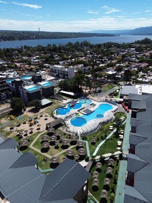 An aerial view of a resort with a large pool area, multiple buildings, and a lake in the background.