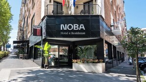 Das Hotel NOBA e Residência: Außenansicht mit moderner Fassade, Sitzgelegenheiten im Freien und mehreren Balkonen.