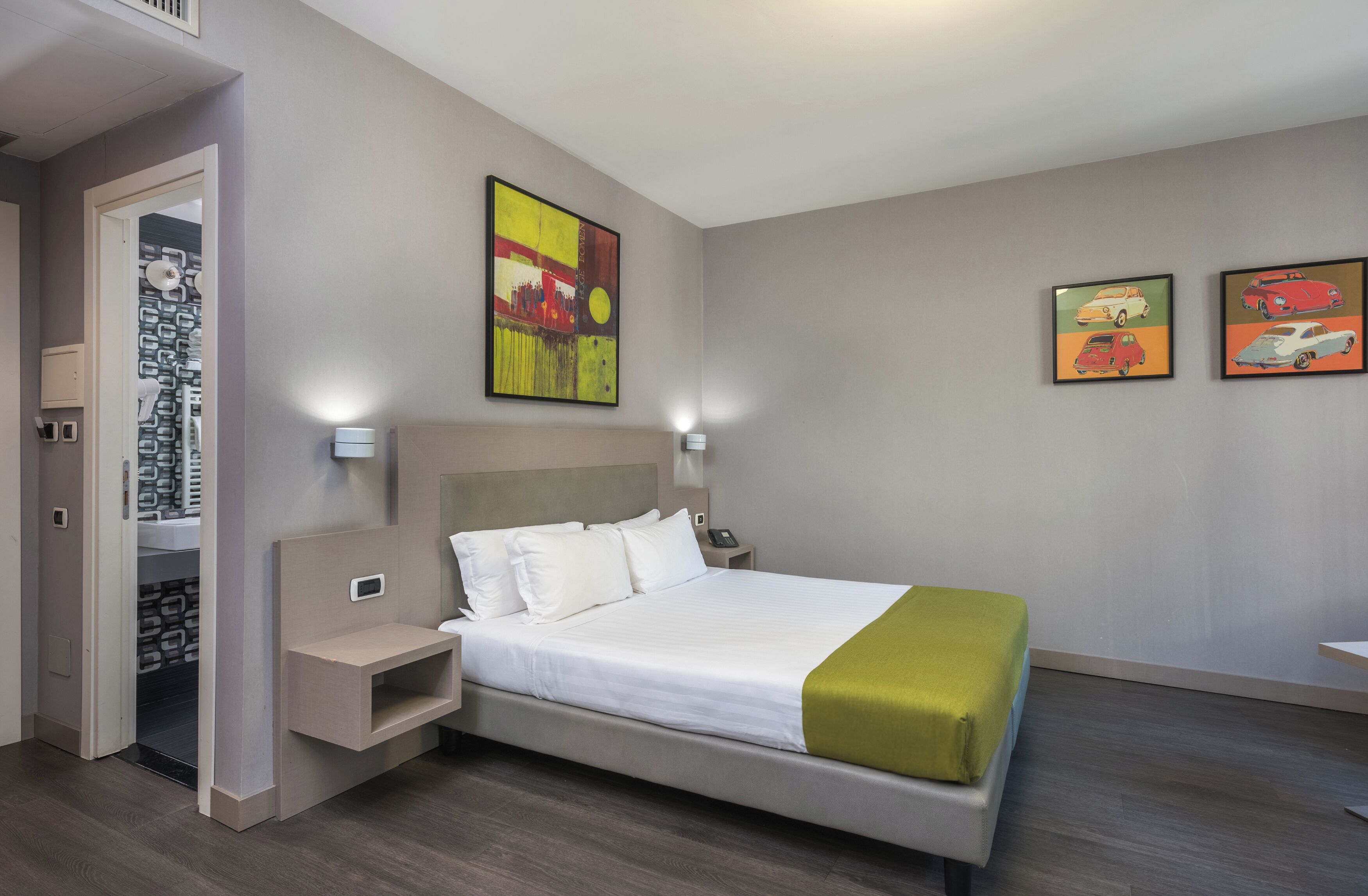 A hotel room with a bed, bedside tables, a nightstand, a wardrobe, and two wall-mounted paintings.