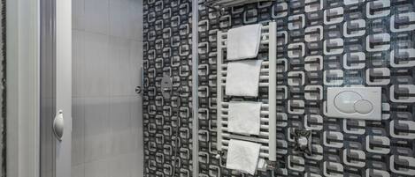 A modern bathroom with a patterned wall, a glass shower enclosure, a white sink, and a towel rack with multiple towels.