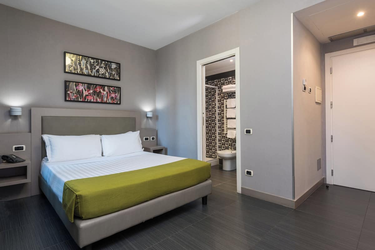 Ett modernt hotellrum med en stor säng, sängbord, ett litet bord och ett badrum som syns genom en öppen dörr.