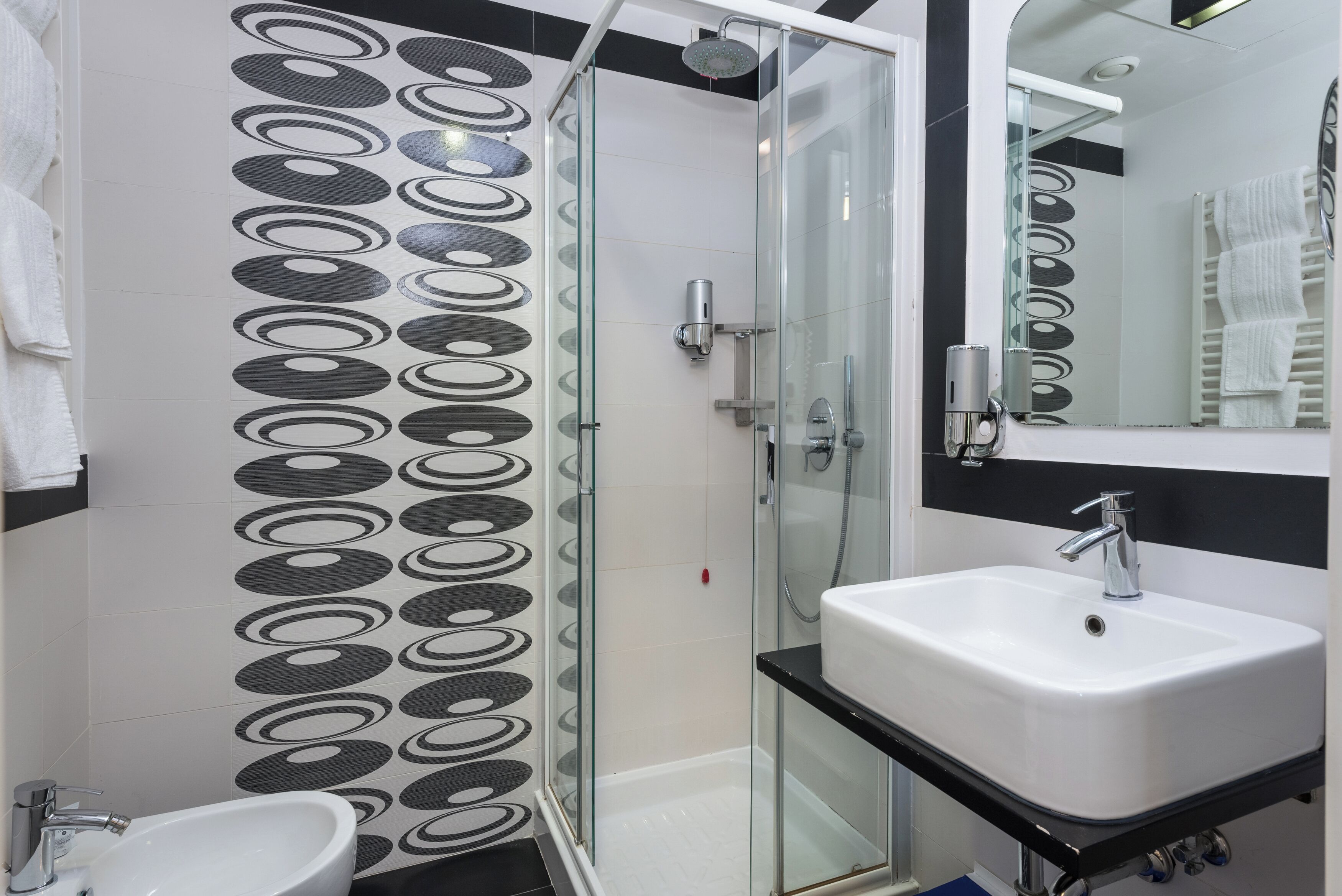 Une salle de bain moderne avec une douche à parois de verre, un lavabo blanc et un grand miroir.