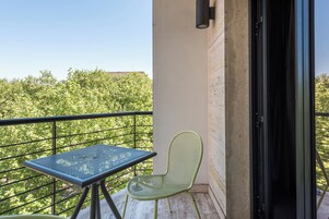 Un balcon avec une table en métal et une chaise verte, une porte et une vue sur les arbres.