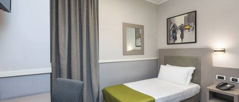 A hotel room with a bed, a bedside table with a phone, a mirror, a painting, and a window with curtains.