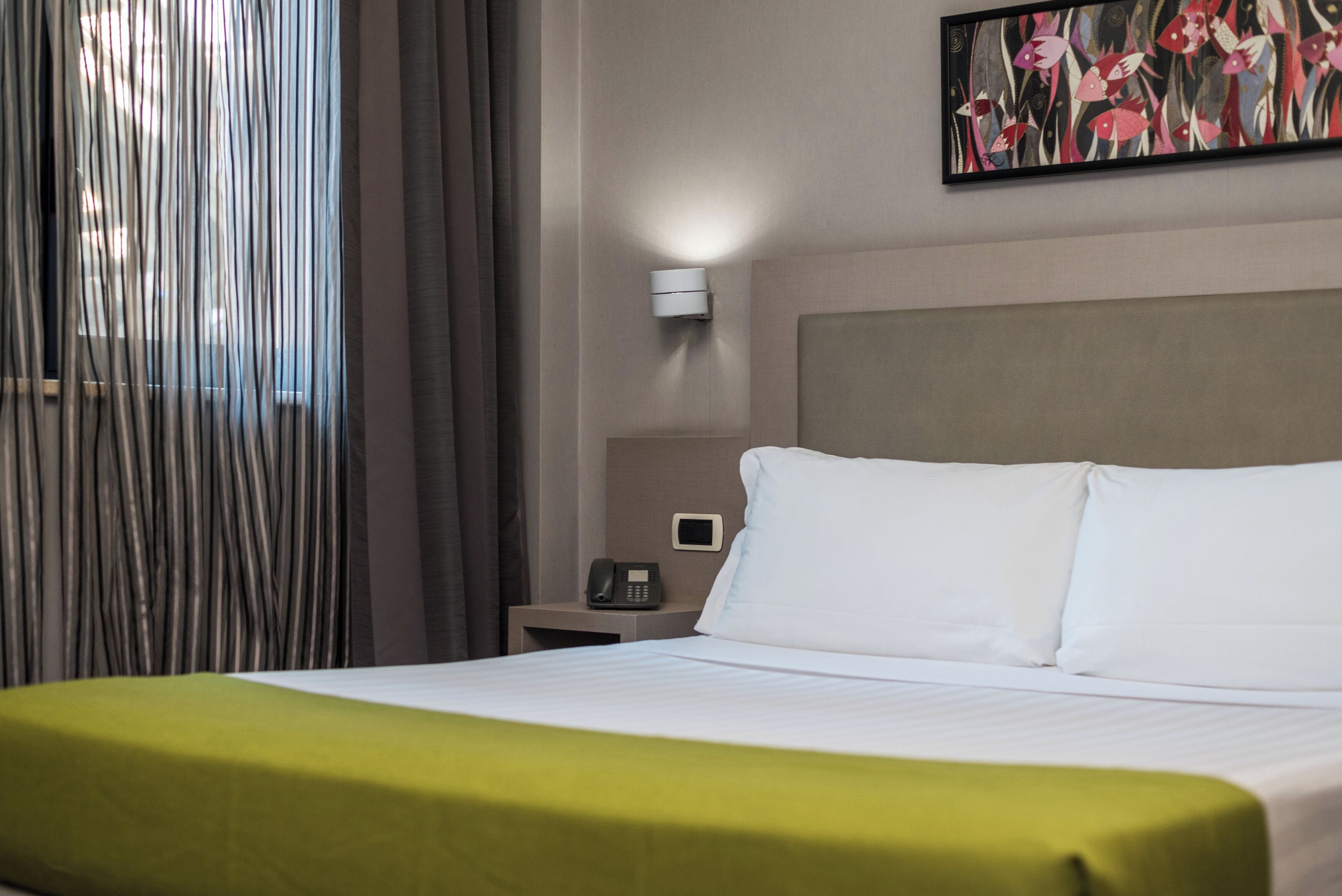Een hotelkamer met een bed, een nachtkastje met een telefoon, een wandlamp en een schilderij.