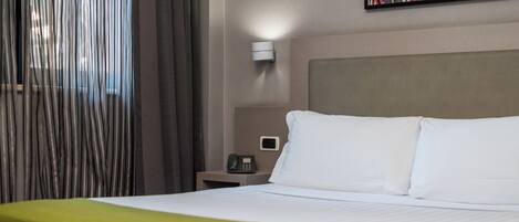 Een hotelkamer met een bed, een nachtkastje met een telefoon, een wandlamp en een schilderij.