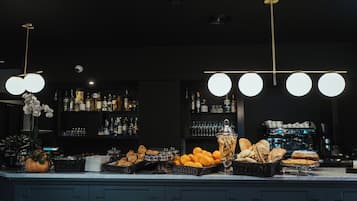 A bar area with a counter displaying pastries, oranges, and a coffee machine.