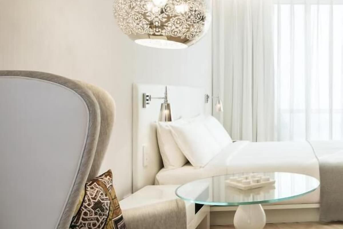 A modern hotel room with a curved armchair, a glass coffee table, and a decorative light fixture.