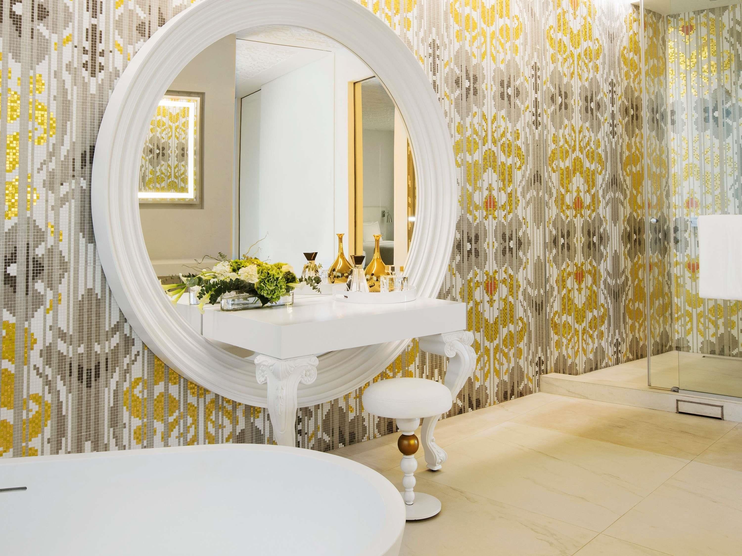 A bathroom with a white vanity, a round mirror, and a white pedestal sink.