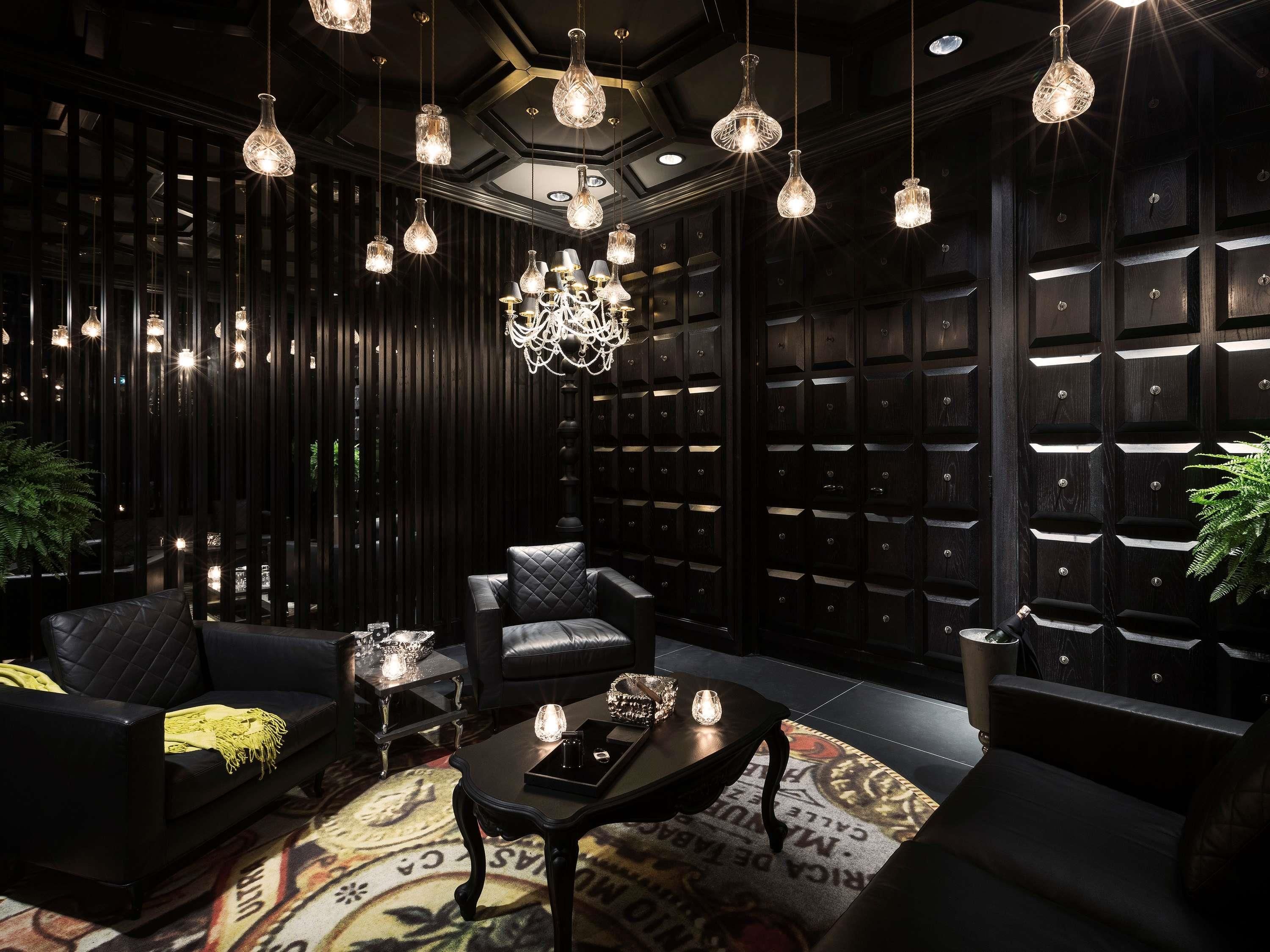 A modern interior with a dark wood panel wall, leather seating, a patterned rug, and multiple hanging light fixtures.