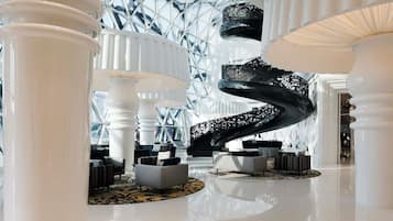 Un vestíbulo moderno con una escalera en espiral, grandes columnas blancas y un techo de vidrio geométrico.