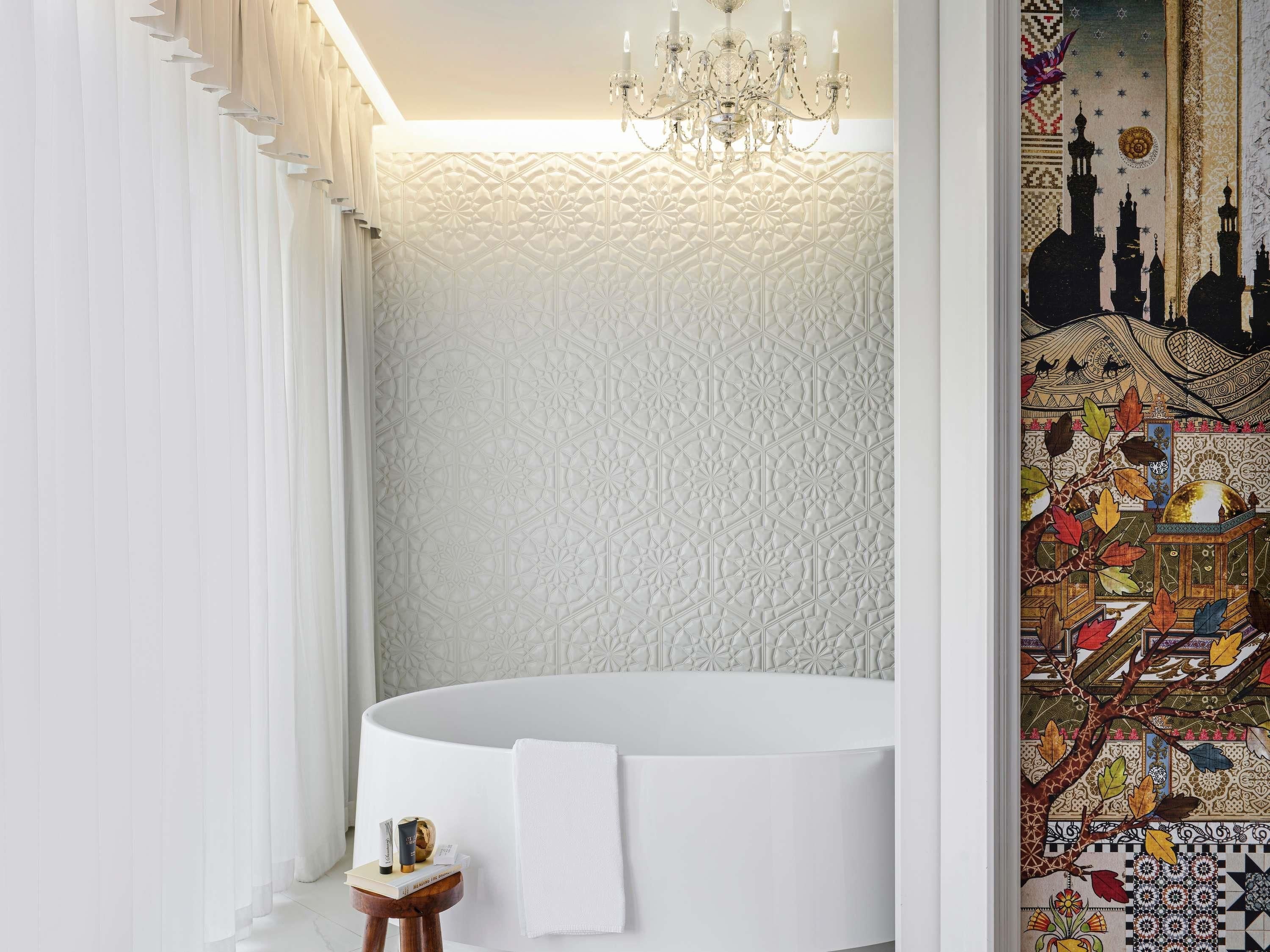 Une salle de bain moderne avec une grande baignoire, un lustre et un mur décoratif orné d’un motif géométrique.