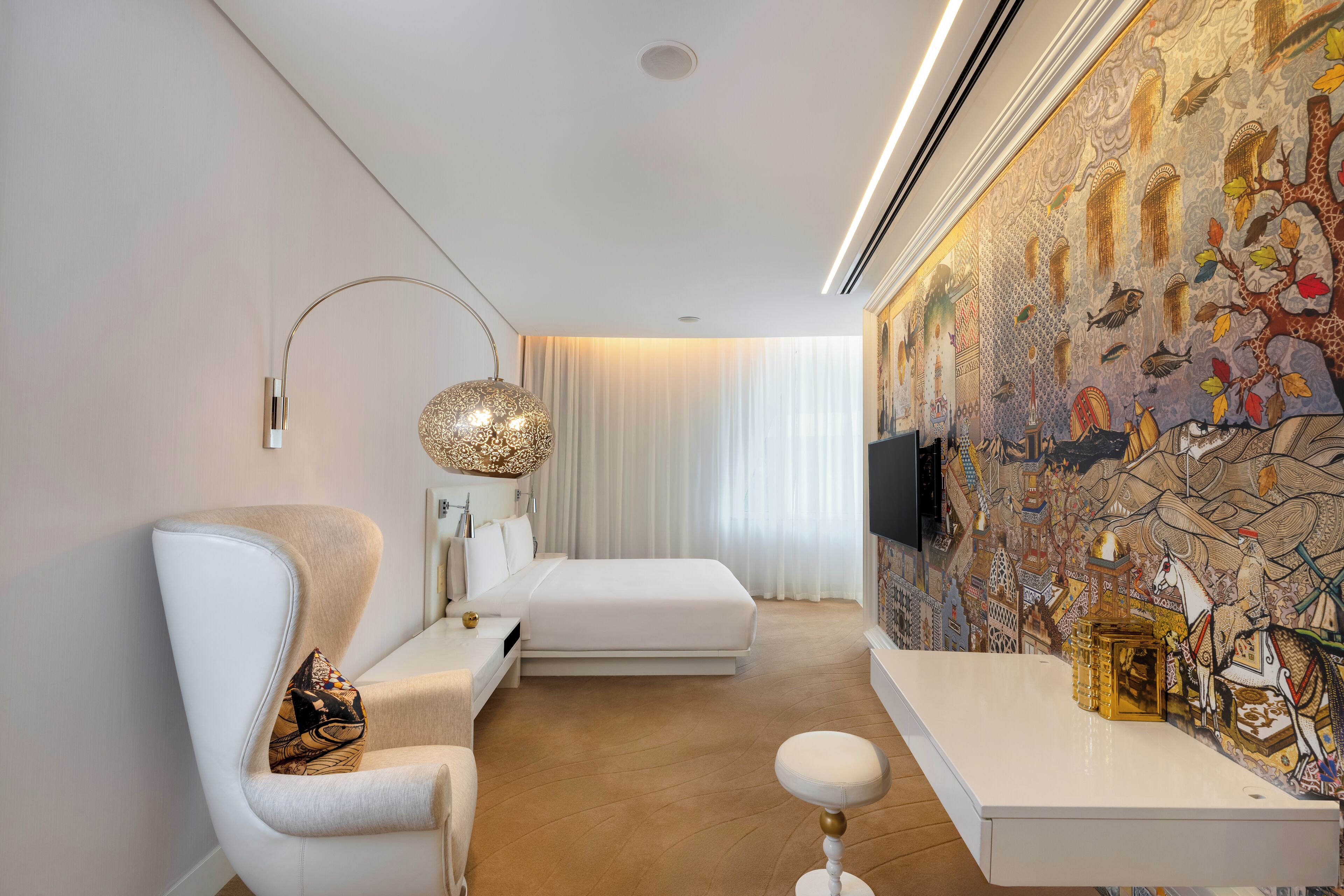 A modern bedroom with a large bed, a white armchair, a small table, and a decorative wall mural.